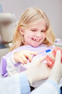 Mädchen übt Zähneputzen an einem Gebiss beim Kinderzahnarzt