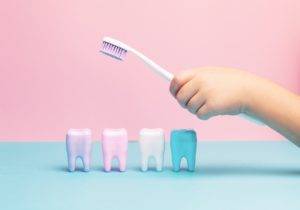 Kinderhand hält Zahnbürste über Modellzähne